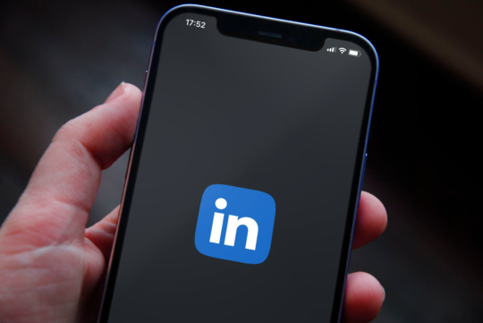 Mão segurando um celular com a logo do Linkedin