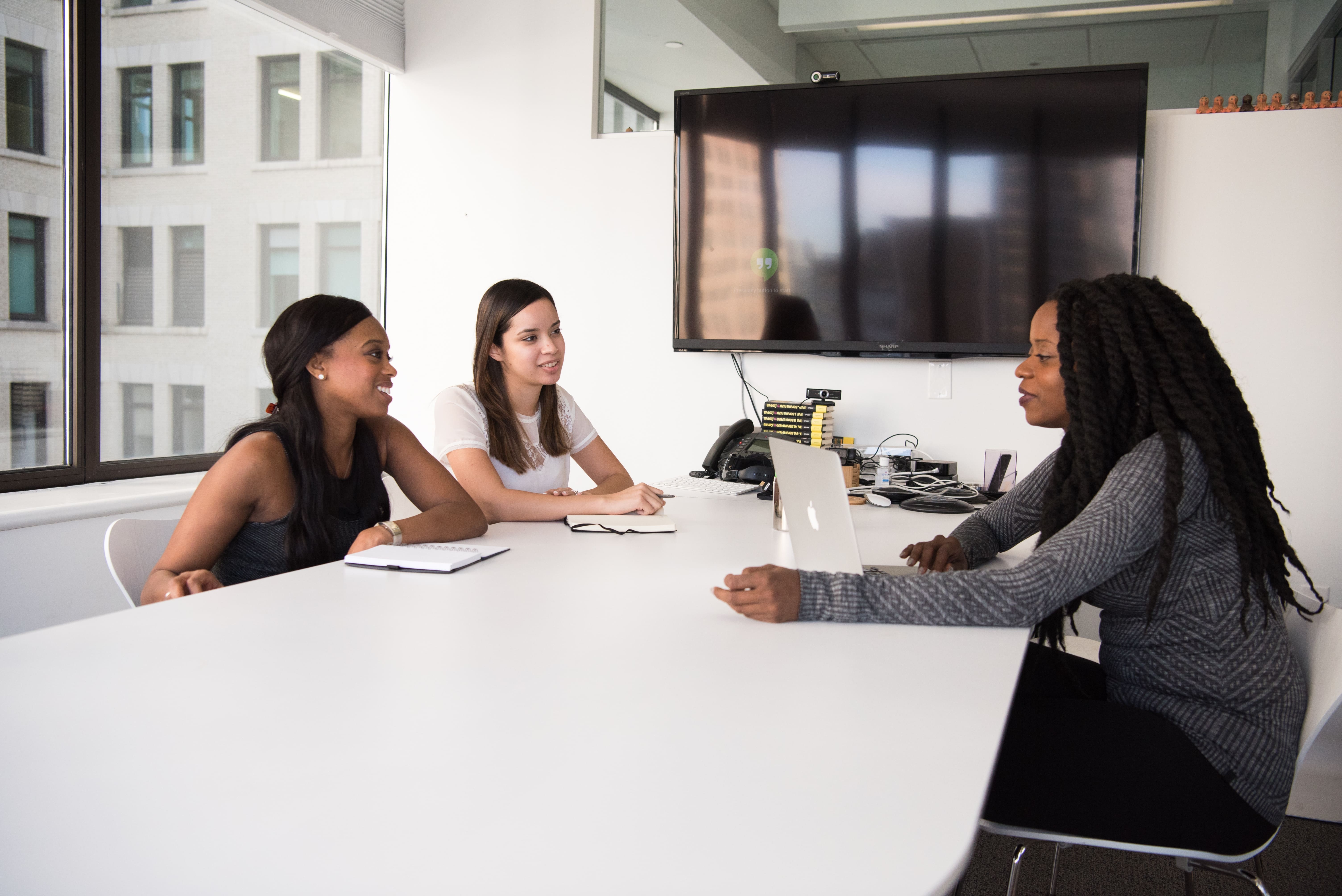 Três mulheres sentadas em uma mesa branca enquanto conversam