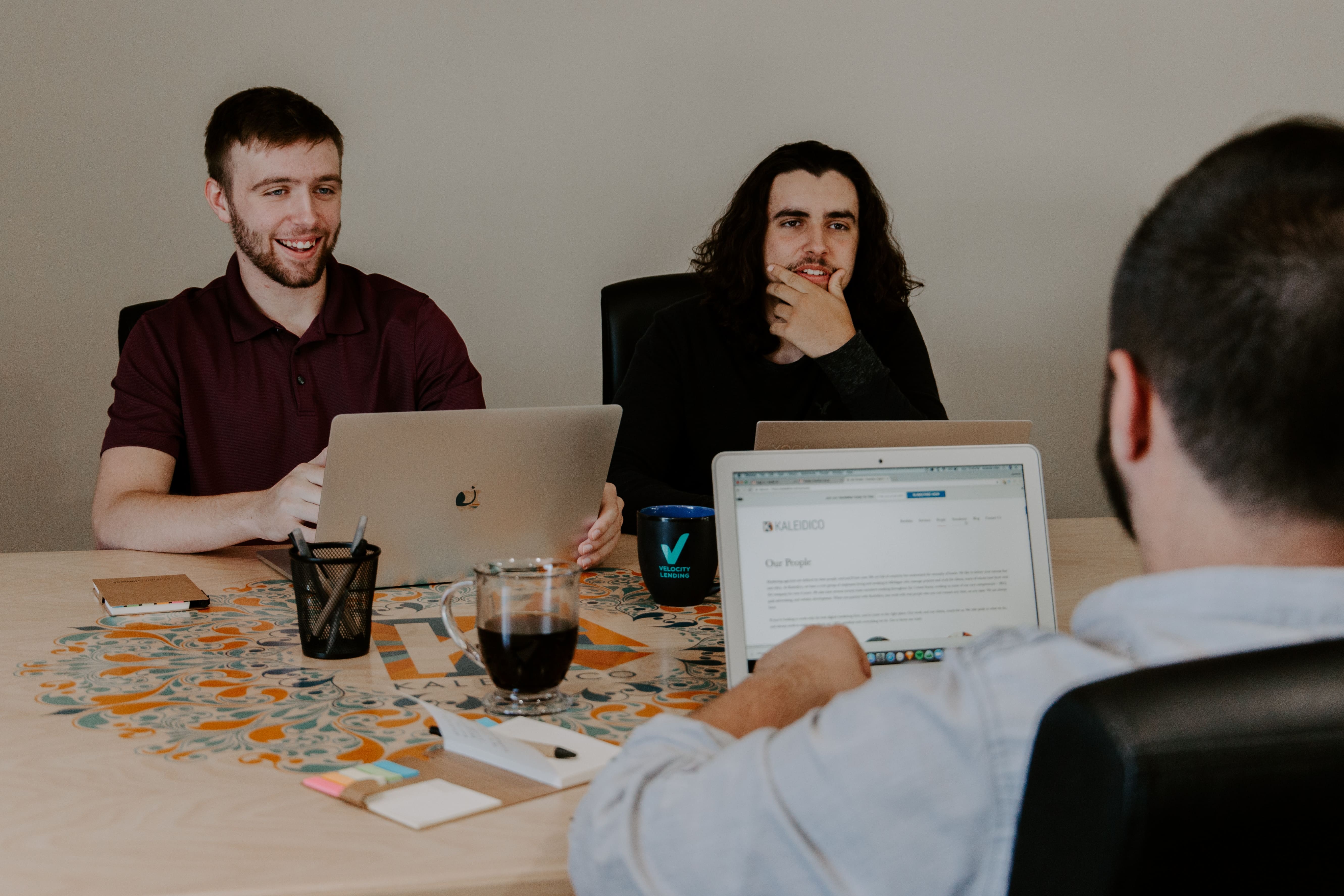 Três pessoas reunidas em uma mesa, conversando com computadores ligados